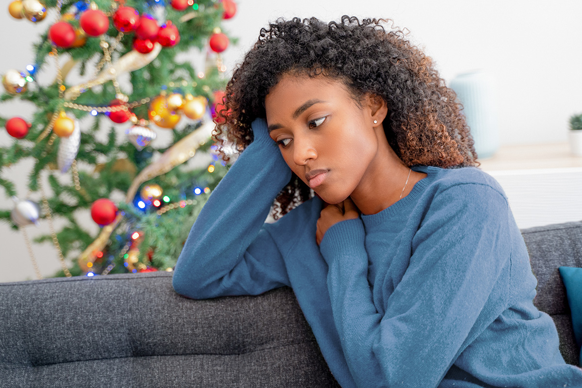 Depressed young woman sitting on a couch with a Christmas tree in the background