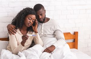 Sad couple sitting on bed with negative pregnancy test result