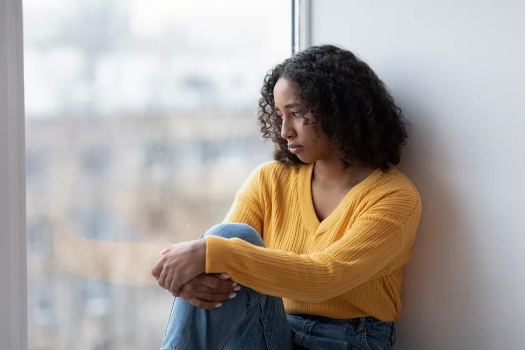 Woman sitting in a window looking anxious.