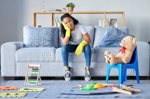 Tired mom sitting on couch surrounded by a mess of childrens toys