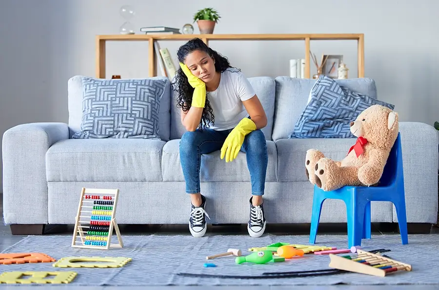 Tired mom sitting on couch surrounded by a mess of children's toys.