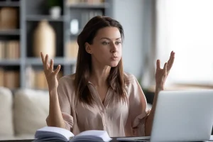 Unhappy young woman looking at laptop screen, irritated by bad gadget work, low internet connection, working remotely at home.