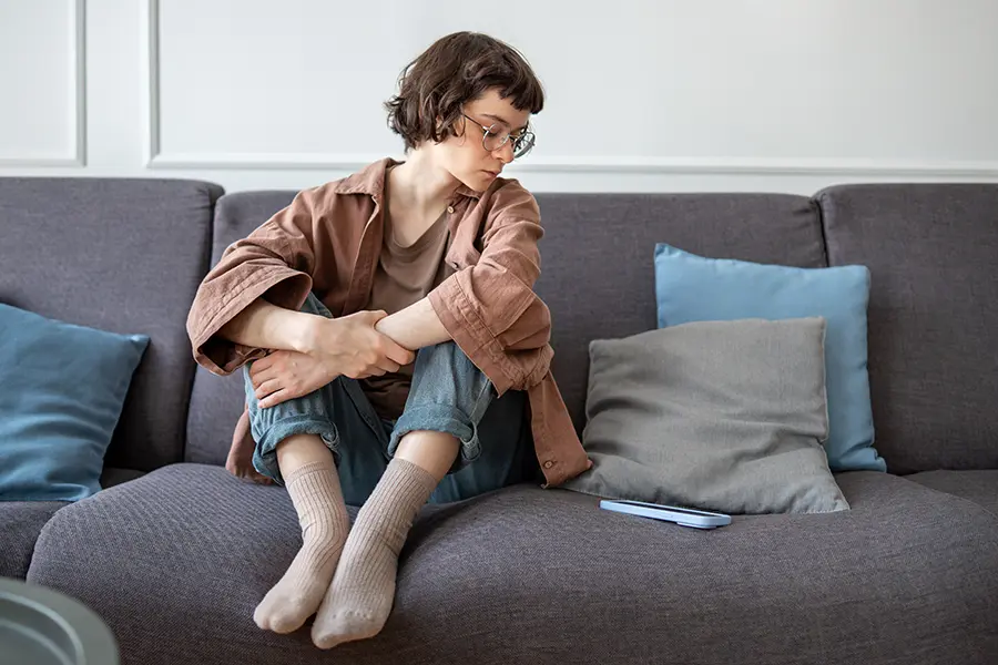 Depressed woman sitting on couch looking at phone