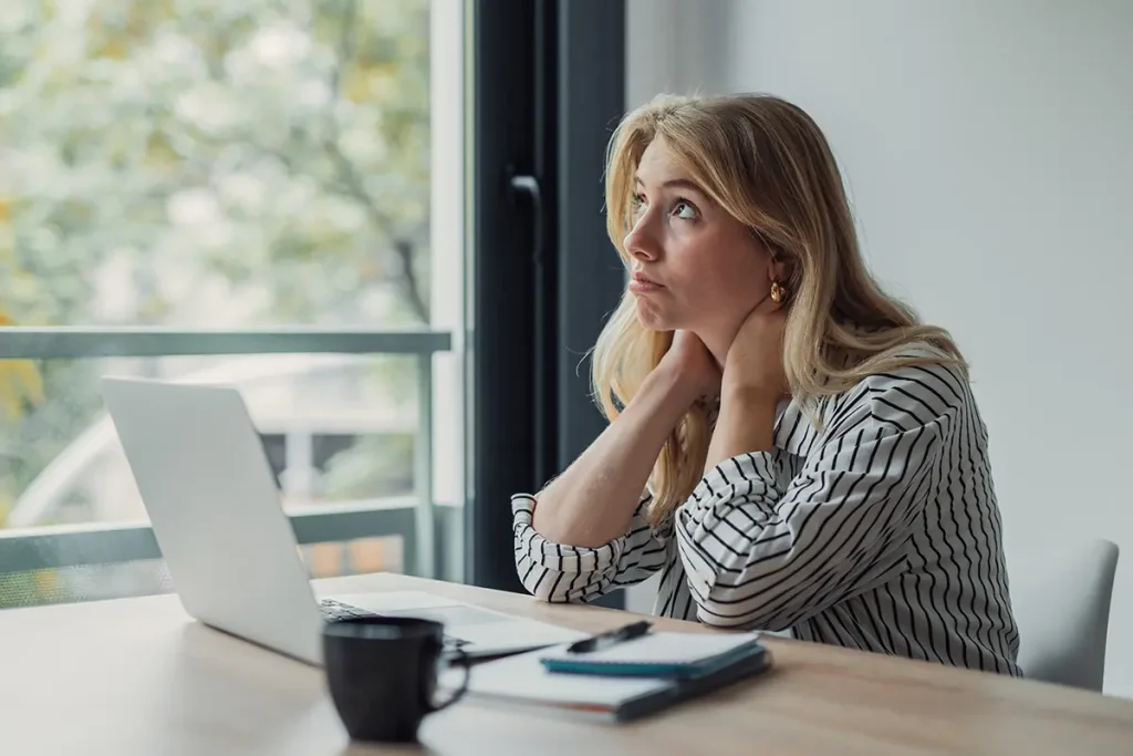 Woman looking out window at a desk with a laptop on it